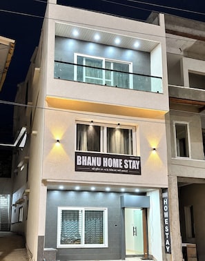Ein zweistöckiges Gebäude mit einem Schild für 'BHANU HOME STAY' und einer sichtbaren Eingangstür.