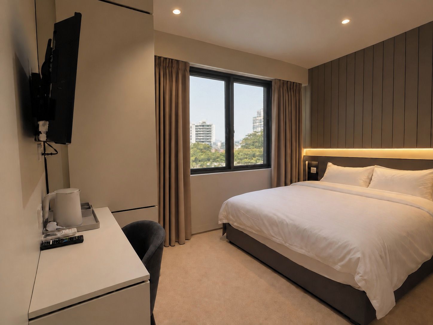 A hotel room with a bed, a desk, a chair, a television mounted on the wall, and a window with curtains.