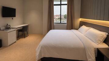 A hotel room with a bed, a desk, a chair, a television, and a window with curtains.