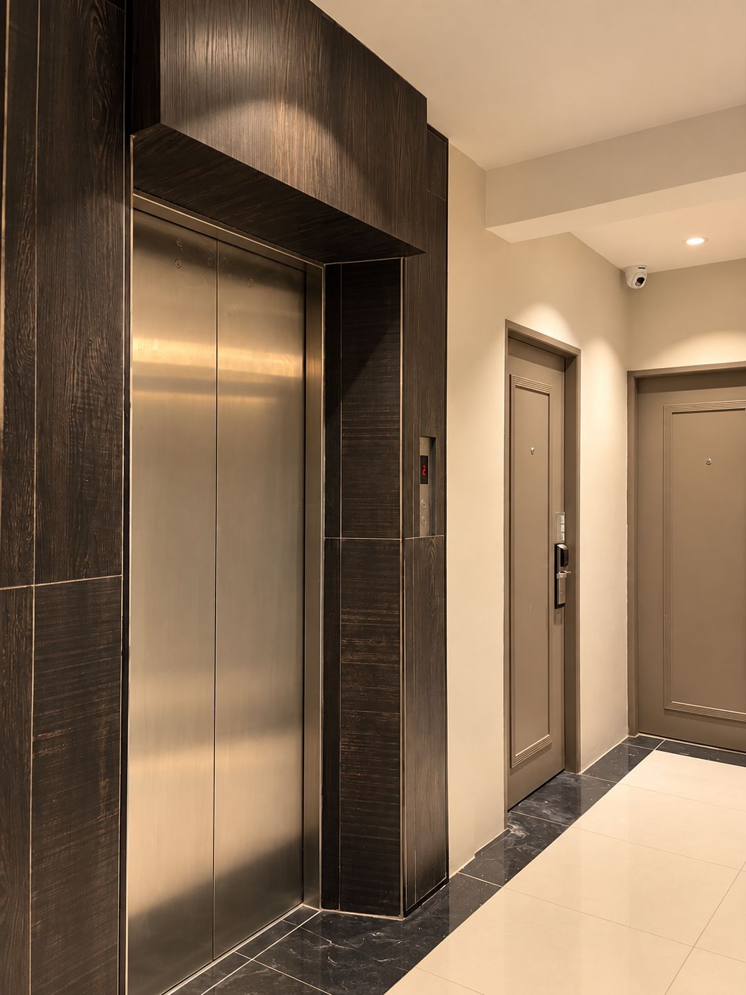 A modern elevator with a metallic finish, flanked by dark wooden panels and a beige wall.
