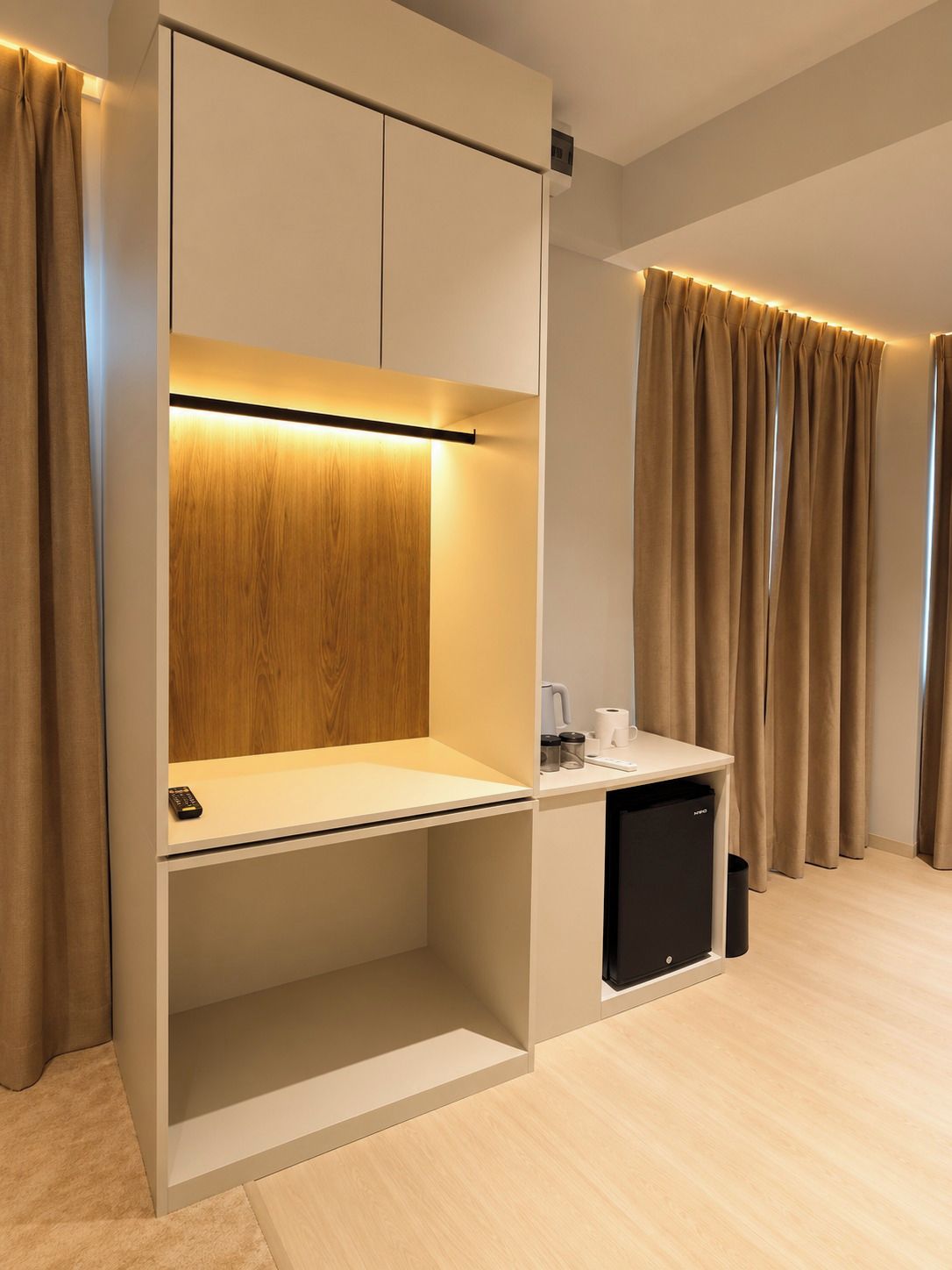 A modern room with a built-in desk, a small black trash bin, and a curtain-covered window.