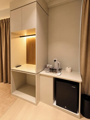 Ein kleines Hotelzimmer mit einer Küchenzeile, einem kleinen Kühlschrank, einer Kaffeemaschine und einer Fernbedienung auf der Ablagefläche.
