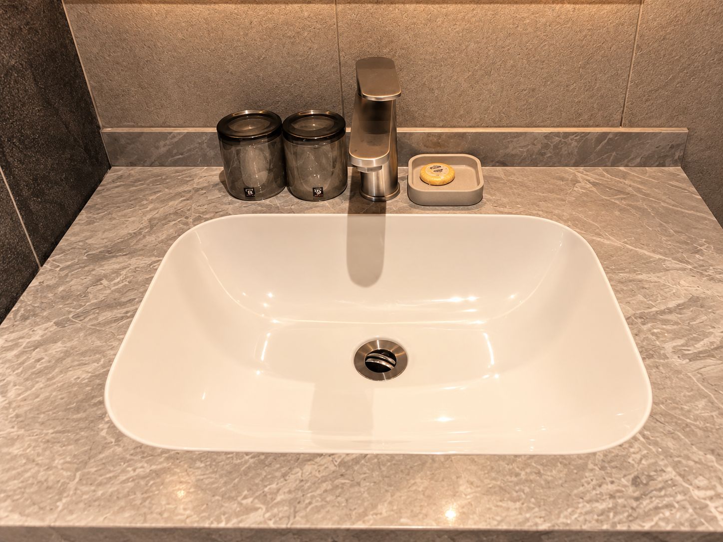 A bathroom sink with a modern faucet, two cylindrical containers, and a soap dish.