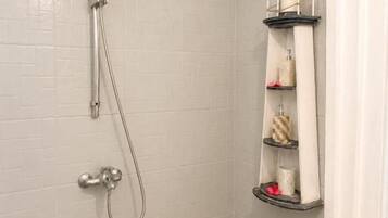 A shower with a handheld showerhead and a wall-mounted shelf with toiletries.