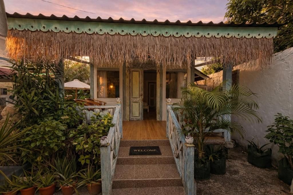 A building with a thatched roof entrance, a wooden staircase, and a welcome mat.