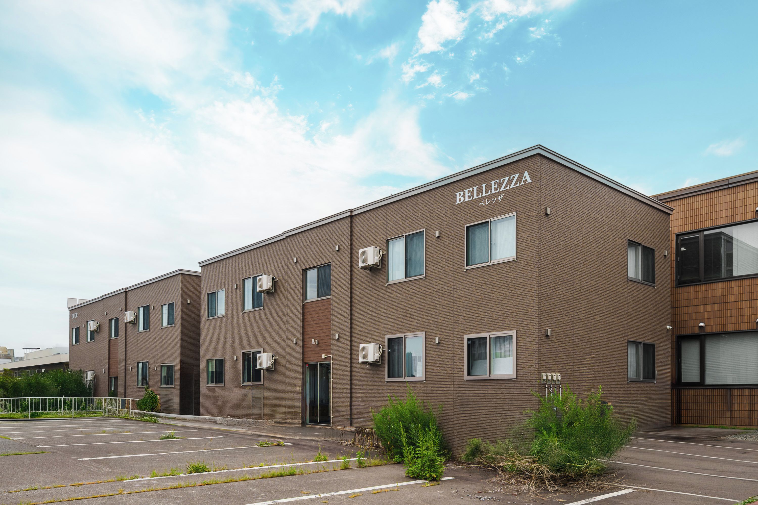 A multi-story building with the name 'BELLEZZA' on the facade, featuring a brick exterior, multiple windows, and air conditioning units.