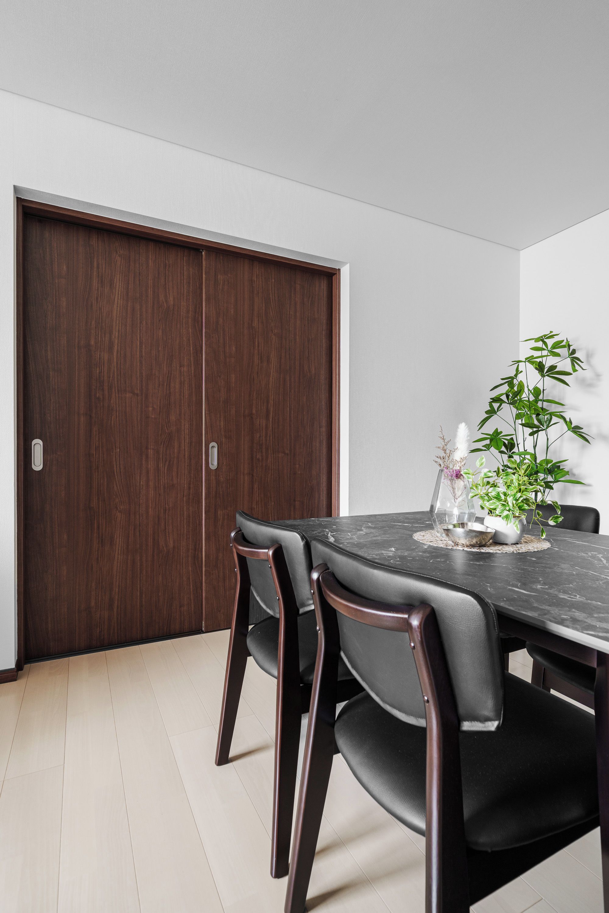 A dining area with a dark wood table, black chairs, and a potted plant.