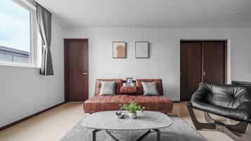A modern living room with a brown sofa, a black leather chair, a round coffee table, and two framed artworks on the wall.