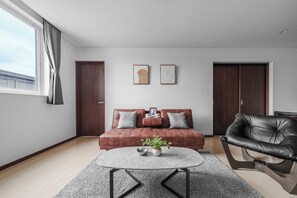 A modern living room with a brown sofa, a black leather chair, a round coffee table, and two framed artworks on the wall. - Bellezza 101 (Asahikawa)