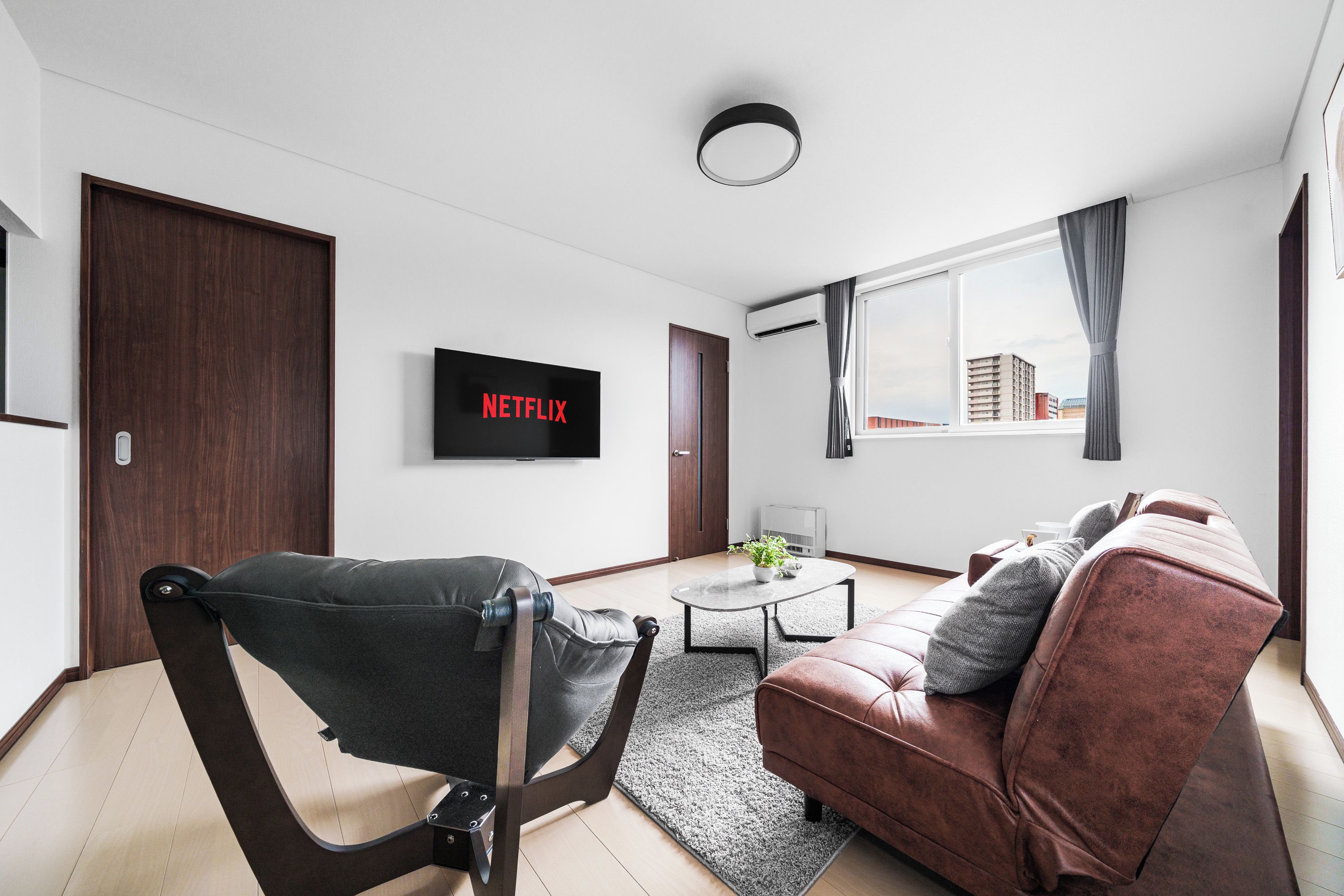 A modern living room with a leather sofa, a black chair, a coffee table, and a flat-screen TV mounted on the wall.