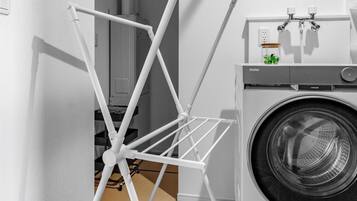 A laundry area with a hanging rack, a washing machine, and a laundry basket.