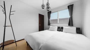 Moderni hotellihuone, jossa on suuri sänky, vaatekaappi, ikkuna verhoilla ja kattovalaisin.