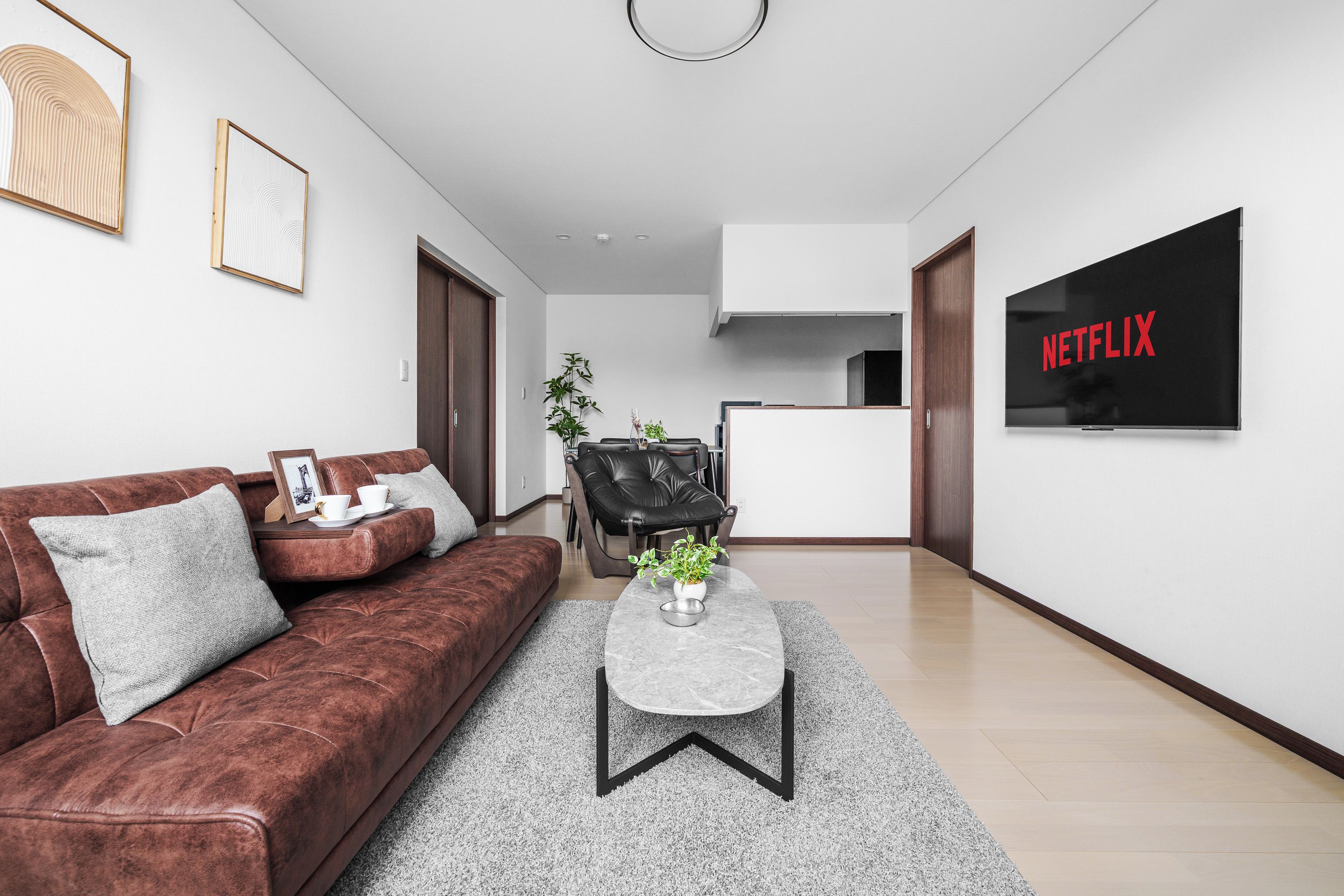 A modern living room with a brown sofa, a coffee table, and a TV displaying 'NETFLIX' in red letters.