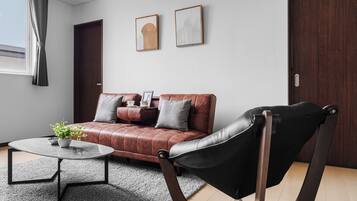 A modern living room with a leather sofa, a black leather chair, a coffee table, and a potted plant.