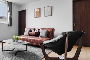Uma sala de estar moderna com um sofá de couro, uma poltrona de couro preta, uma mesa de centro e uma planta em vaso.