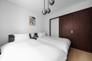 Quarto com cama de casal, mesa de cabeceira com luminária, uma pequena planta e guarda-roupa de madeira.