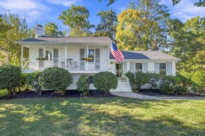 Uma casa de dois andares com varanda, uma bandeira americana e um gramado bem cuidado.