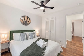 Quarto bem arrumado com cama, abajures, ventilador de teto e um prato decorativo na parede.