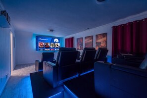 Une salle de cinéma maison équipée d’un grand téléviseur à écran plat affichant l’interface d’un service de diffusion en continu, de plusieurs options de sièges et d’un écran de projection fixé au mur.