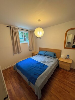 A bedroom with a bed, a nightstand, a bedside lamp, a window with curtains, and a mirror on the wall. - Entire 1BR + Office, Parking & Garden Access aprmt (Longueuil)