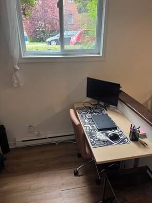 A room with a desk, a computer, and a window overlooking a street. - Entire 1BR + Office, Parking & Garden Access aprmt (Longueuil)