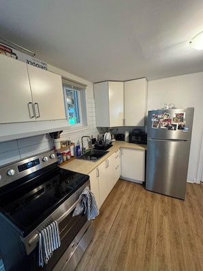 A modern kitchen with stainless steel appliances, white cabinetry, and a wooden floor. - Entire 1BR + Office, Parking & Garden Access aprmt (Longueuil)