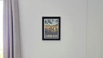 Une photo encadrée du désert de Saint-Gulik, accrochée à un mur blanc, un canapé gris et une fenêtre avec des rideaux gris.