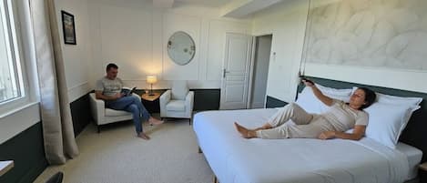 Een hotelkamer met een bed, een zithoek met een fauteuil, een nachtkastje en een spiegel aan de muur.