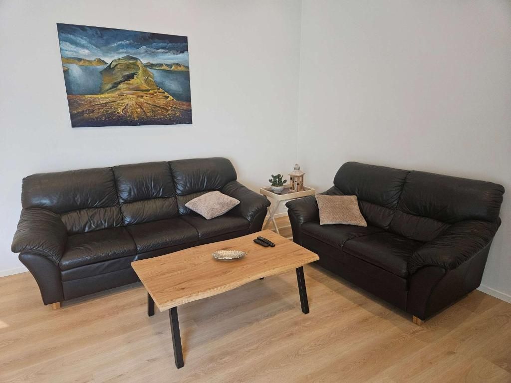 Ein Wohnzimmer mit zwei schwarzen Ledersofas, einem Holztisch und einem Bild an der Wand.