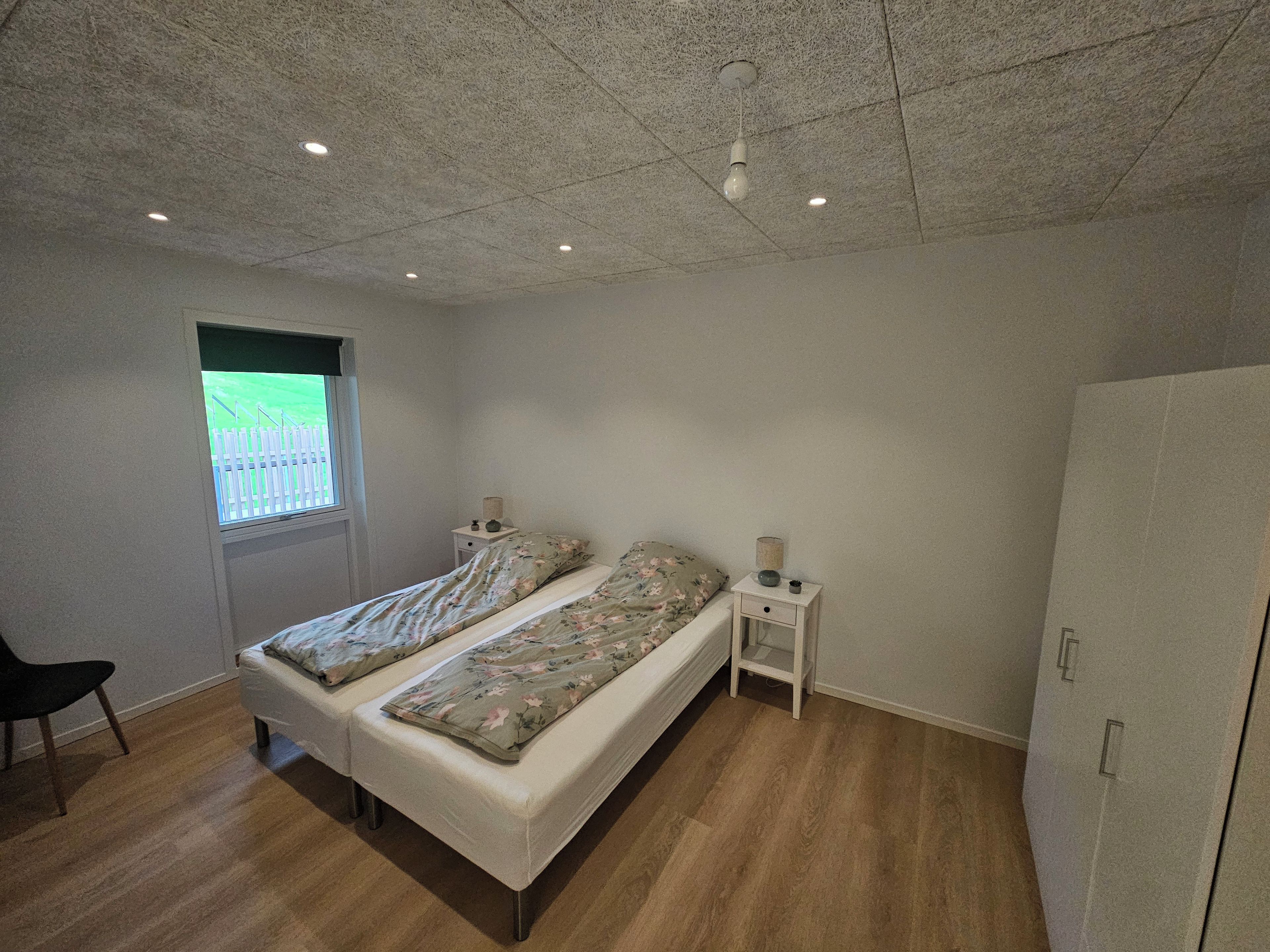 Ein Schlafzimmer mit zwei Betten, einem Fenster, einem Kleiderschrank und einem Nachttisch mit einer Lampe.