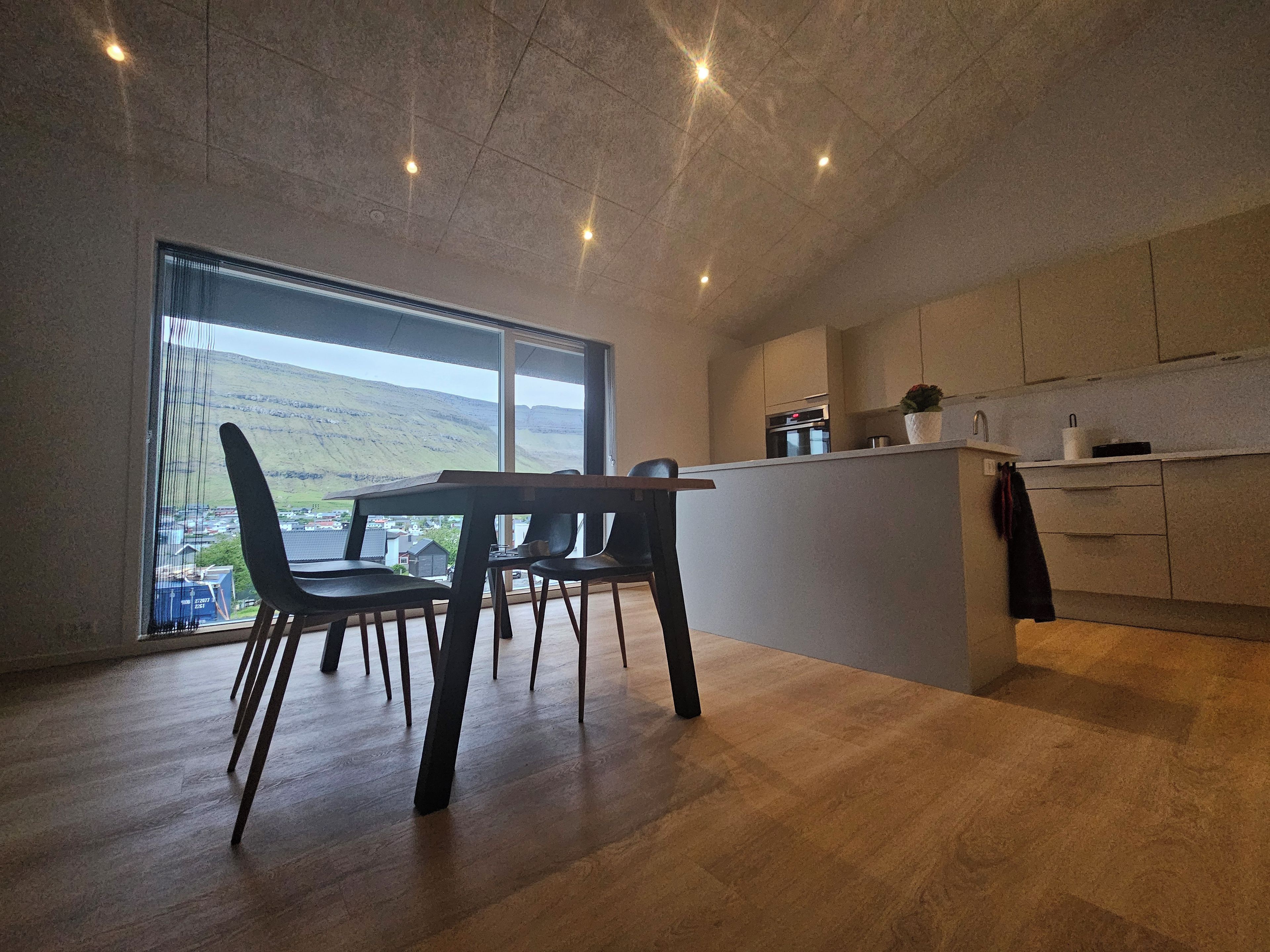 Cozinha moderna com área de refeições, grandes janelas e vista para uma paisagem montanhosa.