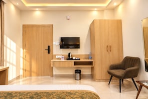 A hotel room with a bed, a desk with a TV, a chair, and a wardrobe. - Darpan Nikunj (Vrindavan)