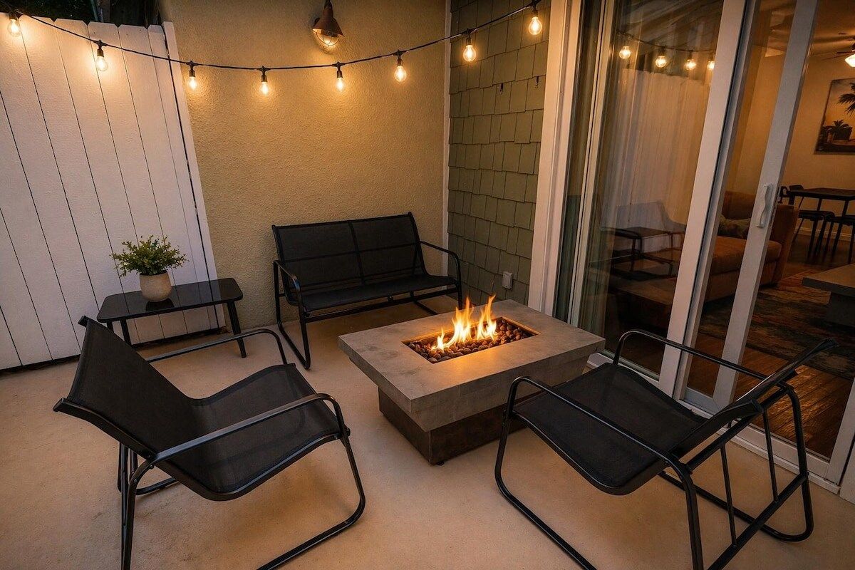 An outdoor seating area with a fire pit, chairs, and string lights.