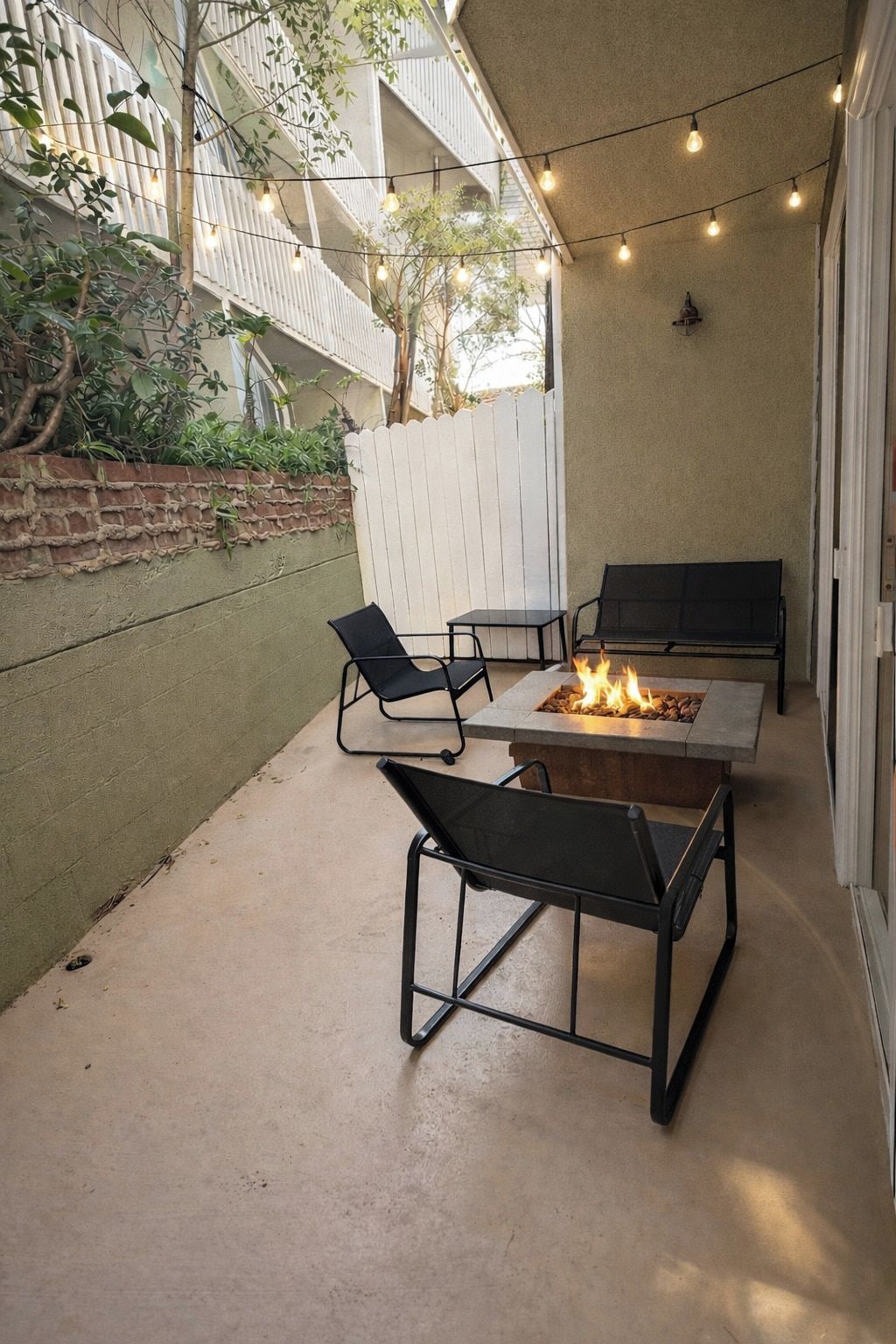 Een terras buiten met een vuurkuil, twee stoelen en een tafel.