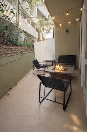 Een terras buiten met een vuurkuil, twee stoelen en een tafel.