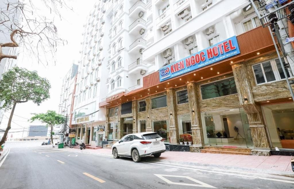 Un hotel con un letrero llamativo, un coche blanco estacionado al frente y vista a la calle.
