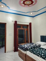 Un dormitorio con cama, ventana con cortinas, techo con detalles decorativos y una puerta.