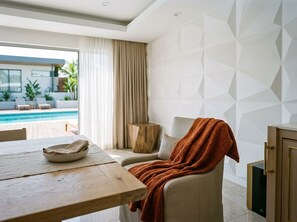 A modern living room with a pool view, a wooden table, and a beige sofa. - Spacious 4-bedroom house in tranquil Minneapolis with AC and gym (Minneapolis)