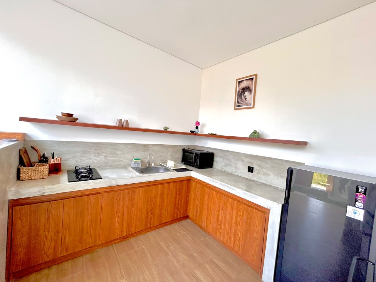 Una cocina con armarios de madera, microondas, lavamanos y refrigerador.