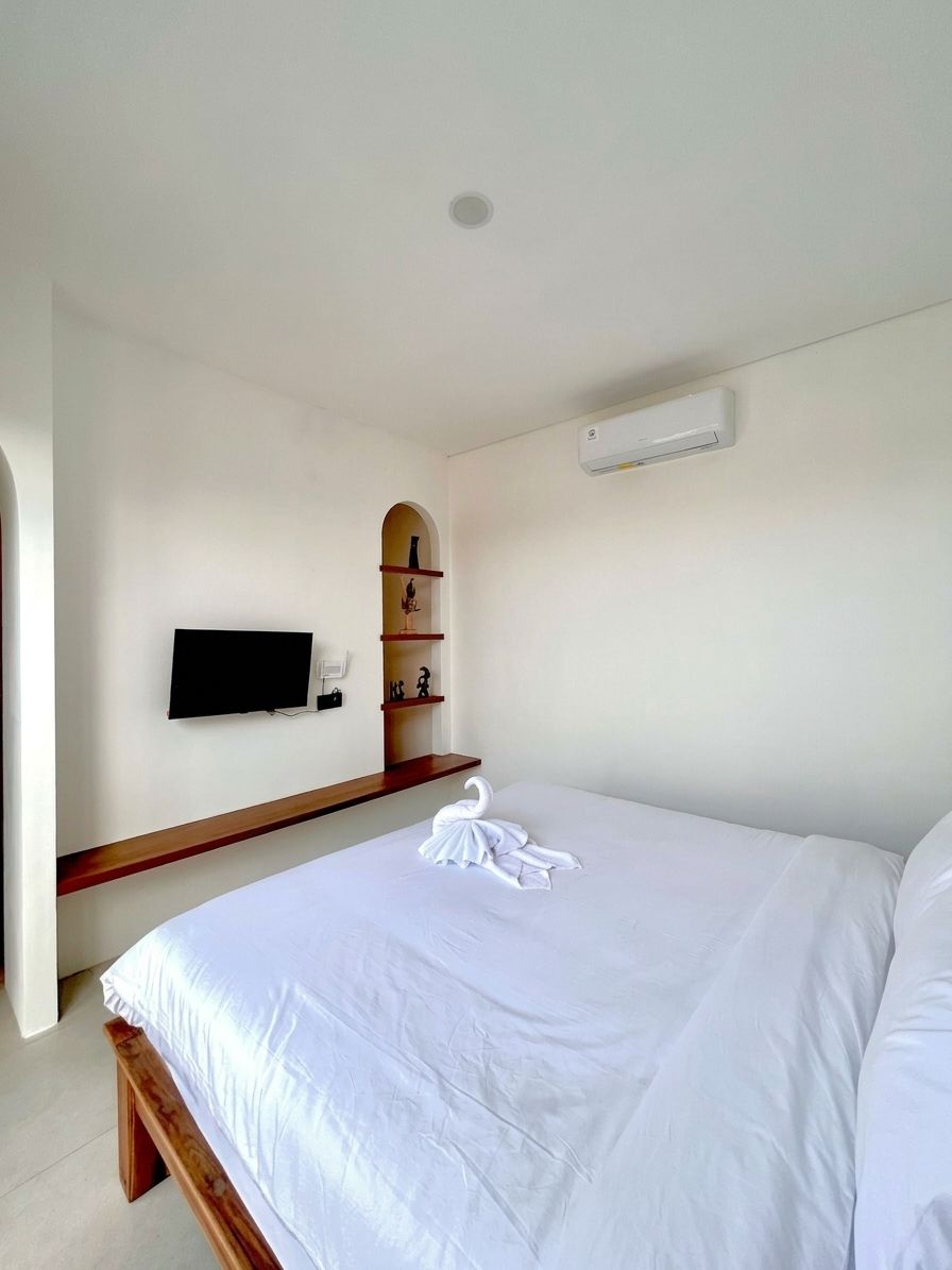 Habitación de hotel con cama, televisor de pantalla plana montado en la pared, estante con adornos y unidad de aire acondicionado instalada en el techo.
