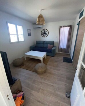 A living room with a sofa, a coffee table, a clock, and a window. - The Blue Tamarisk Fisherman's Cottage (Port-Saint-Louis-du-Rhône)