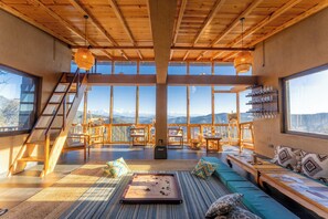 Amplia habitación con un gran ventanal, vigas de madera en el techo y vistas a las montañas.