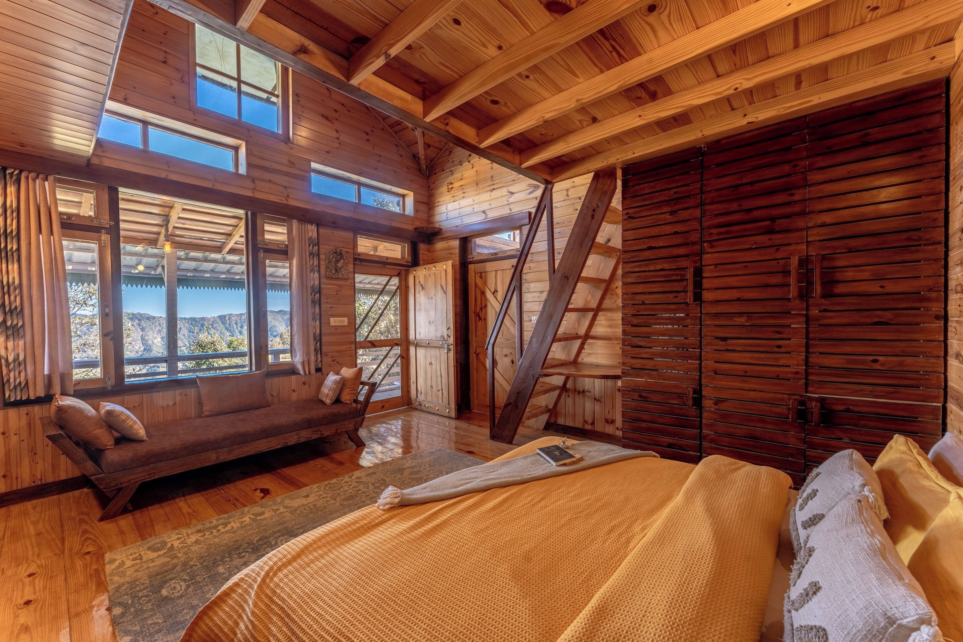 A wooden cabin interior with a bed, a bench, and a view of the outdoors.