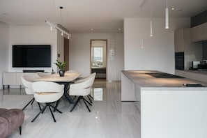 Una cocina moderna con una isla central, comedor con sillas y un televisor de pantalla plana montado en la pared.