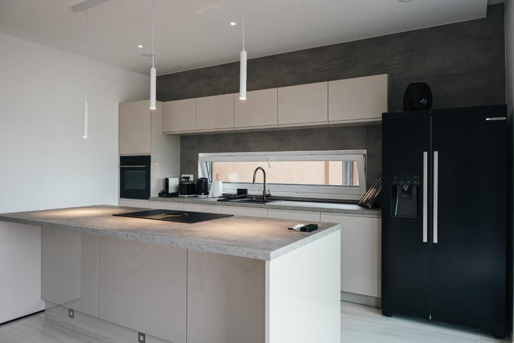 Une cuisine moderne dotée d’un îlot central, d’un réfrigérateur noir et de luminaires suspendus.
