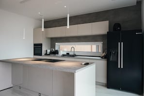 A modern kitchen with a central island, black refrigerator, and pendant lighting. - Prestige Rooftop Apartments Viva (Maribor)