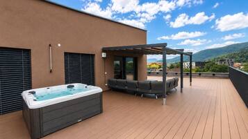 A rooftop deck with a hot tub, outdoor seating, and a pergola.