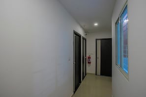 Un pasillo estrecho con paredes blancas, suelo de baldosas y puertas a ambos lados.