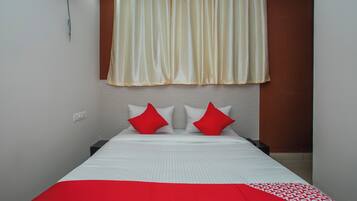 Una habitación de hotel con una cama, dos almohadas, una colcha roja y blanca, una cortina y un aire acondicionado de pared.
