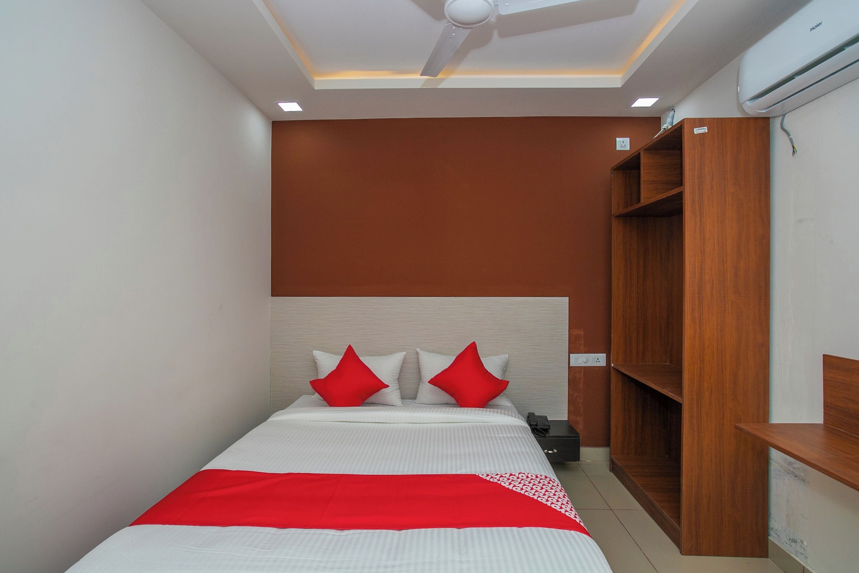 A hotel room with a bed, a ceiling fan, recessed lighting, a wooden wardrobe, and a built-in shelf.